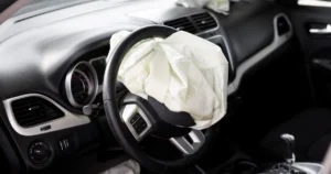 Interior of a car with deployed airbag, the steering wheel is black with silver accents, the dashboard is black, the car seats are black, the car is a Dodge Journey.