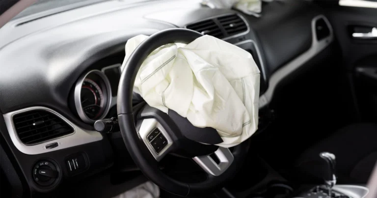 Interior of a car with deployed airbag, the steering wheel is black with silver accents, the dashboard is black, the car seats are black, the car is a Dodge Journey.