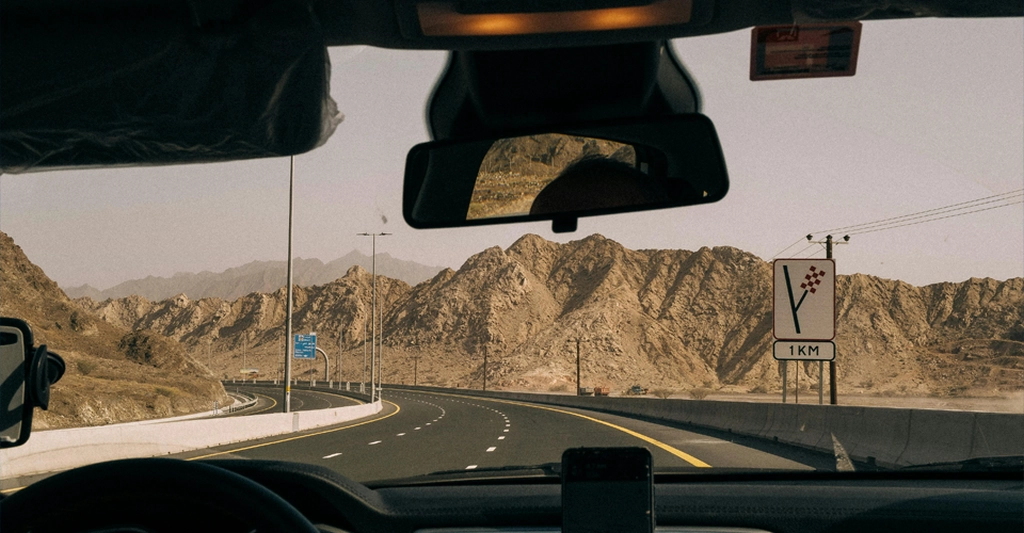 A view from inside a car driving on a highway through a mountainous desert landscape