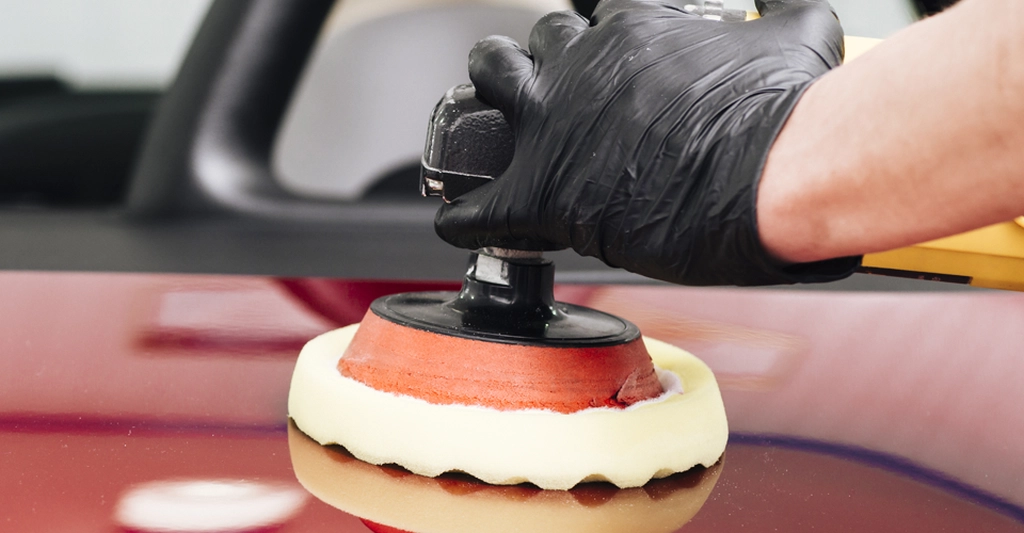 Close-up shot of a gloved hand holding a car polisher on a red car surface.