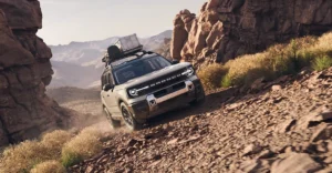 A tan Ford Bronco Sport is angled down a rocky, dusty slope, with a mountain range visible in the background.