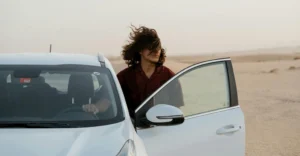 A medium shot captures a 25-year-old Middle Eastern women with light brown skin, standing next to a white car