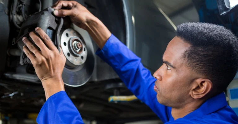 a 32-year-old Black man in a blue mechanic's uniform, focused on repairing a car's brake system.