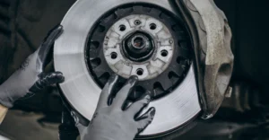 Close-up of a car's brake disc and caliper being inspected by gloved hands.