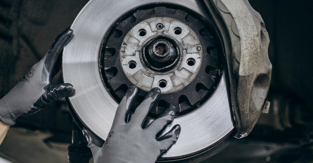 Close-up of a car's brake disc and caliper being inspected by gloved hands.