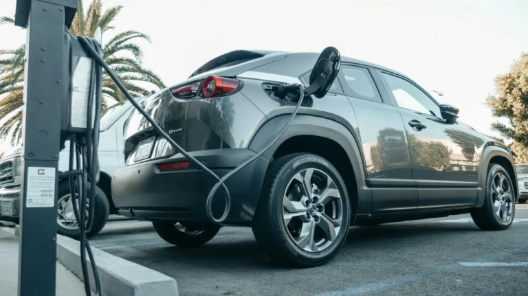 A low-angle shot captures a gray Mazda MX-30 electric vehicle charging at a public charging station