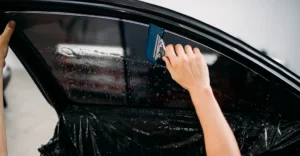 A close-up shot captures the process of tinting a car window, with a fair-skinned person's hands visible.