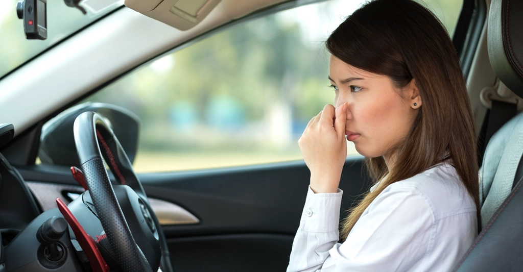 A medium shot depicts an Asian woman, around 25 years old, inside a car, pinching her nose with her right hand.