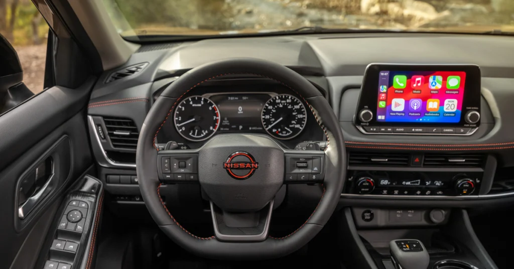 Interior view of a 2026 Nissan Rogue e-Power car with a steering wheel, digital dashboard displaying gauges, and a touchscreen showing app icons. The design is sleek and tech-focused.