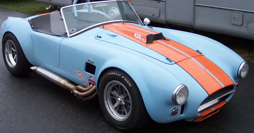 A blue and orange AC Cobra (1962) sports car featuring a prominent white stripe along its side