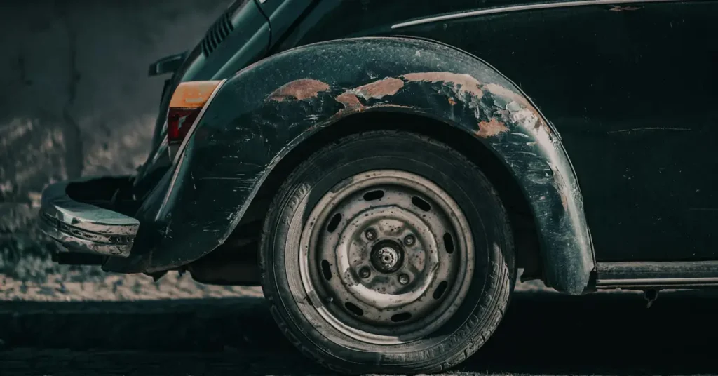 Close-up shot of the rear wheel and fender of a dark green vintage Volkswagen Beetle, showing signs of wear and rust, the paint is peeling off the fender, revealing patches of rust underneath
