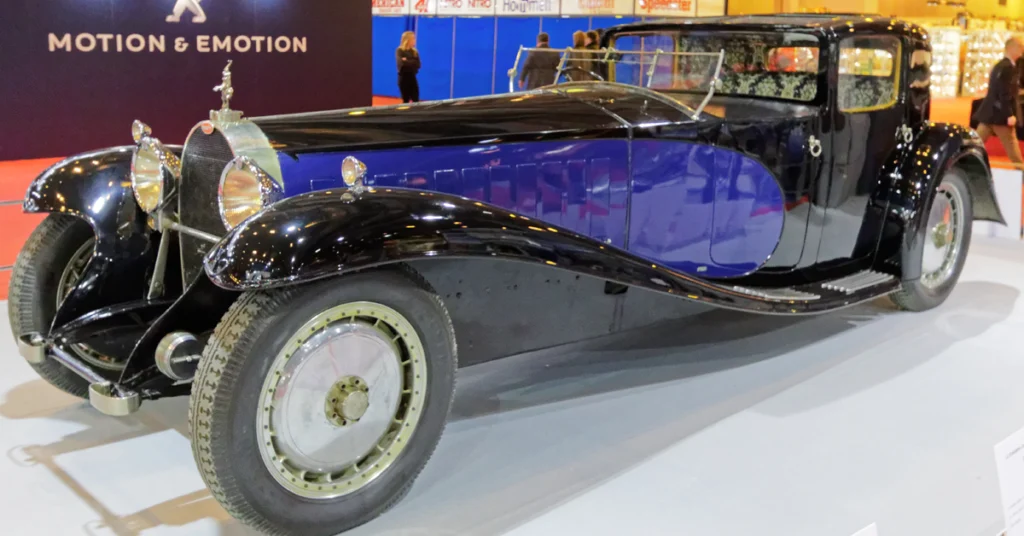 Vintage black and blue Bugatti Royale (1927) luxury car with sleek curves displayed indoors. Elegant and classic design evokes nostalgia and sophistication.