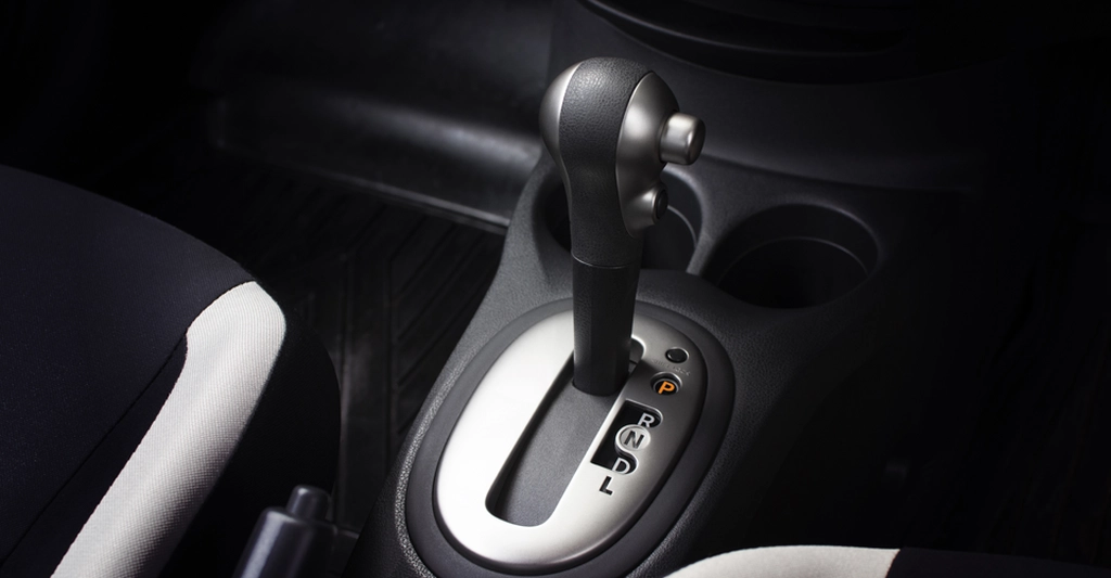 A close-up shot of a car's automatic gear shift, featuring a black and silver gear stick positioned in the center of the frame.