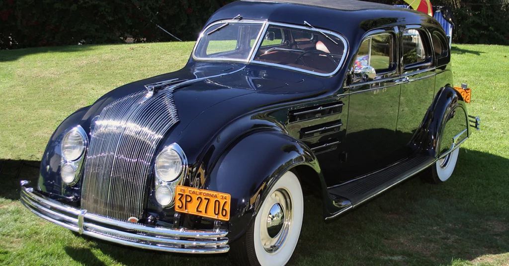 Shiny black vintage Chrysler Airflow (1934) car with chrome detailing, whitewall tires, and a 1934 California license plate, parked on grass, radiating elegance and nostalgia.