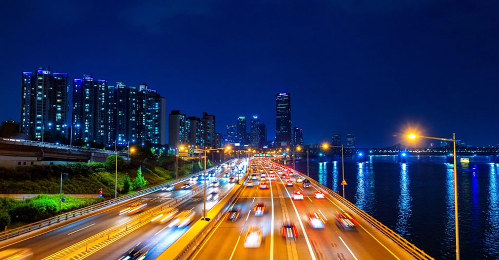 Night Dubai cityscape featuring a multi-lane highway filled with blurred streaks of car headlights and taillights, suggesting heavy traffic