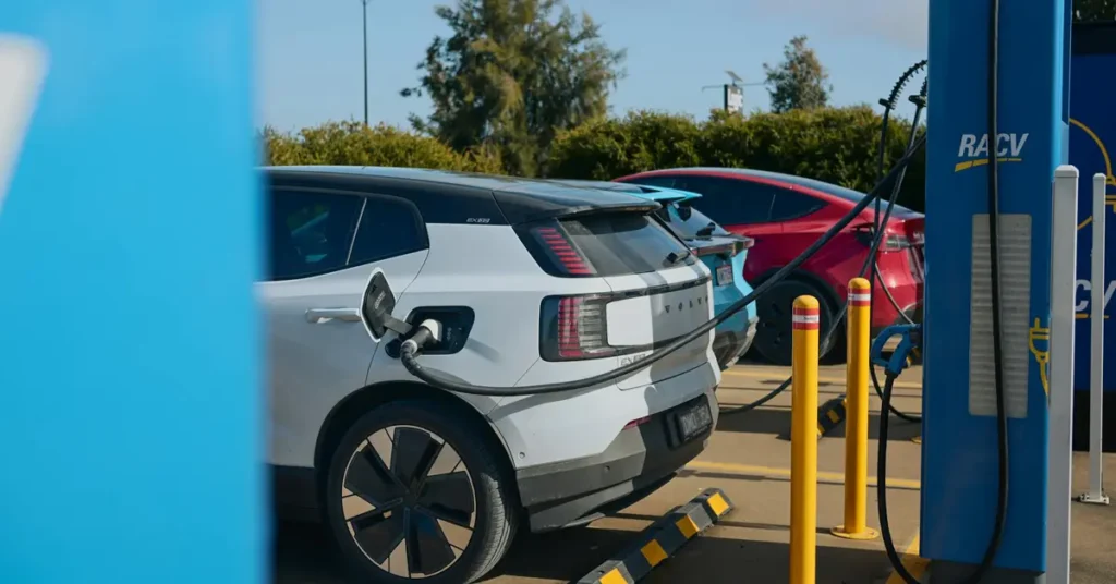 Electric cars are plugged into a charging station, with multiple vehicles lined up for charging.