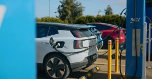 Electric cars are plugged into a charging station, with multiple vehicles lined up for charging.