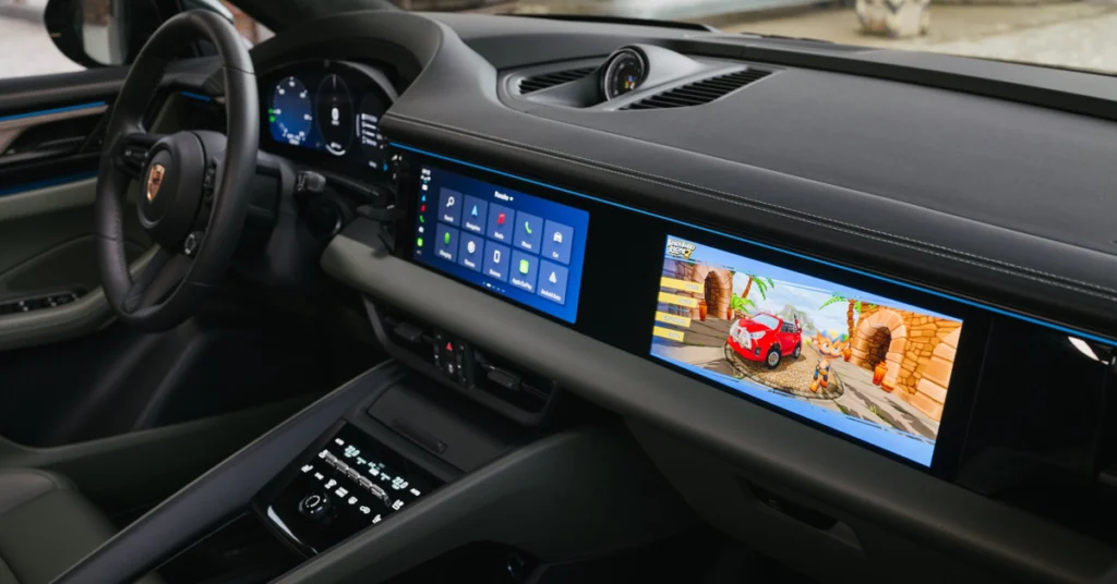Porsche Macan EV luxury car interior featuring a sleek dashboard with dual digital screens: one displaying a game with a red car, the other showing control icons. Modern and high-tech ambiance.