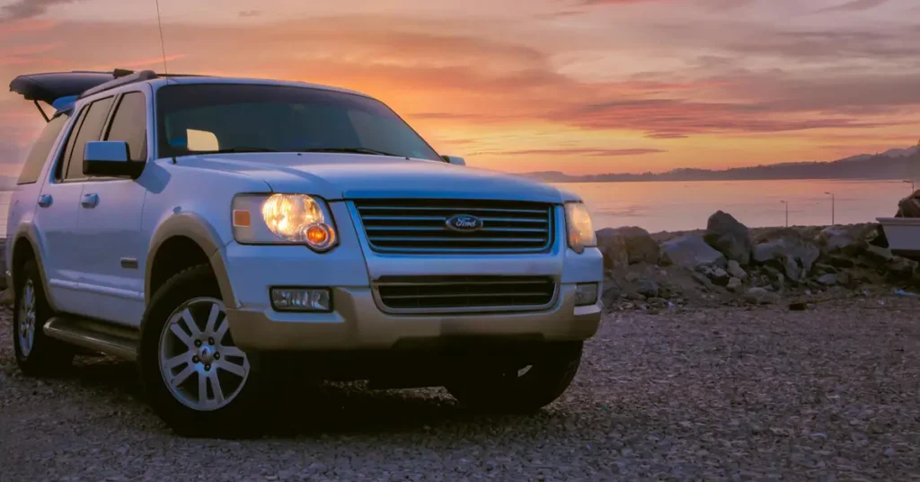 A white Ford SUV parked on the beach, silhouetted against a vibrant sunset sky.