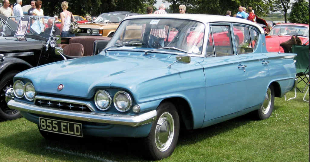A sky-blue vintage Ford Consul Classic (1961) car with a white roof on display at an outdoor car show. Surrounded by people and classic cars, the scene feels nostalgic and lively.