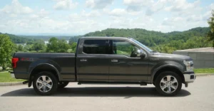 A gray Ford F-150 pickup truck is parked on a paved surface, with a scenic backdrop of rolling green hills and a cloudy sky.