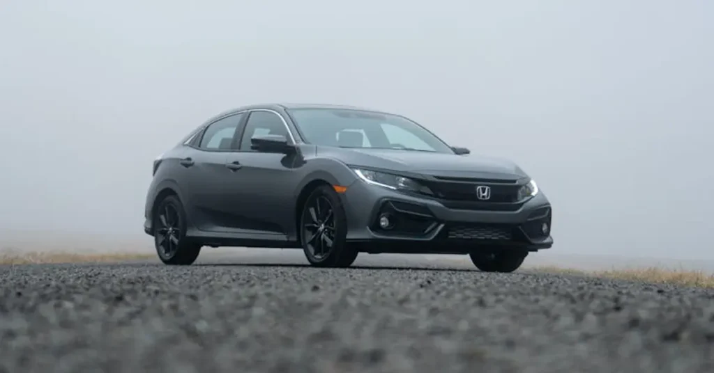 A 2020 Honda Civic hatchback drives along a foggy road, surrounded by mist and blurred trees in the background.