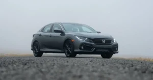 A 2020 Honda Civic hatchback drives along a foggy road, surrounded by mist and blurred trees in the background.