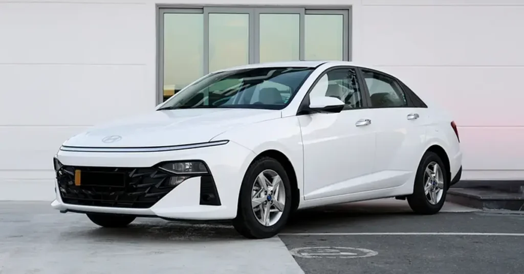 A white Hyundai sedan is parked in front of a white building with a large window