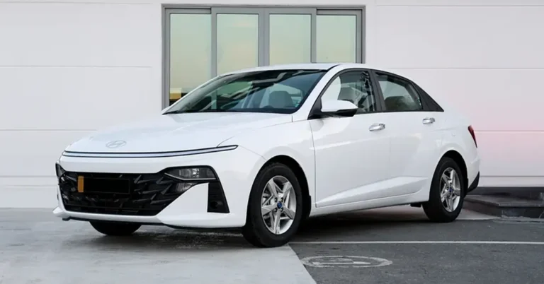 A white Hyundai sedan is parked in front of a white building with a large window