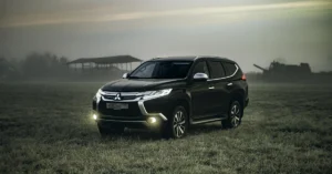 A black A black SUV with headlights on, parked in a foggy field at dusk. The background features faint silhouettes of farm machinery and a barn, creating a moody atmosphere SUV with headlights on, parked in a foggy field at dusk. The background features faint silhouettes of farm machinery and a barn, creating a moody atmosphere