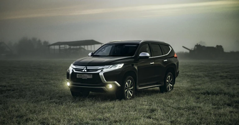 A black A black SUV with headlights on, parked in a foggy field at dusk. The background features faint silhouettes of farm machinery and a barn, creating a moody atmosphere SUV with headlights on, parked in a foggy field at dusk. The background features faint silhouettes of farm machinery and a barn, creating a moody atmosphere