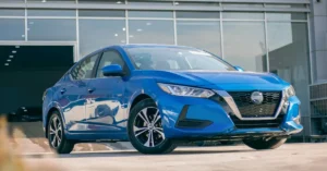 A new Nissan Sunny parked in front of a modern building, showcasing its sleek design and vibrant color.