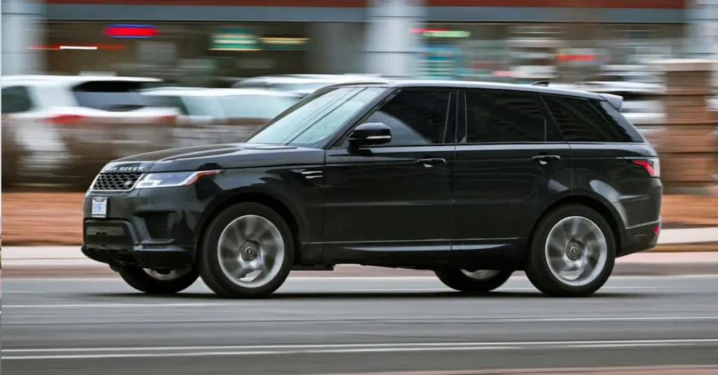 A black Land Rover drives down a city street, surrounded by buildings and trees.