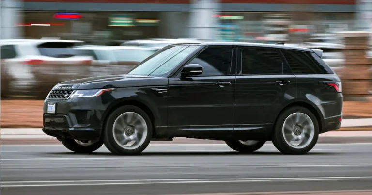 A black Land Rover drives down a city street, surrounded by buildings and trees.