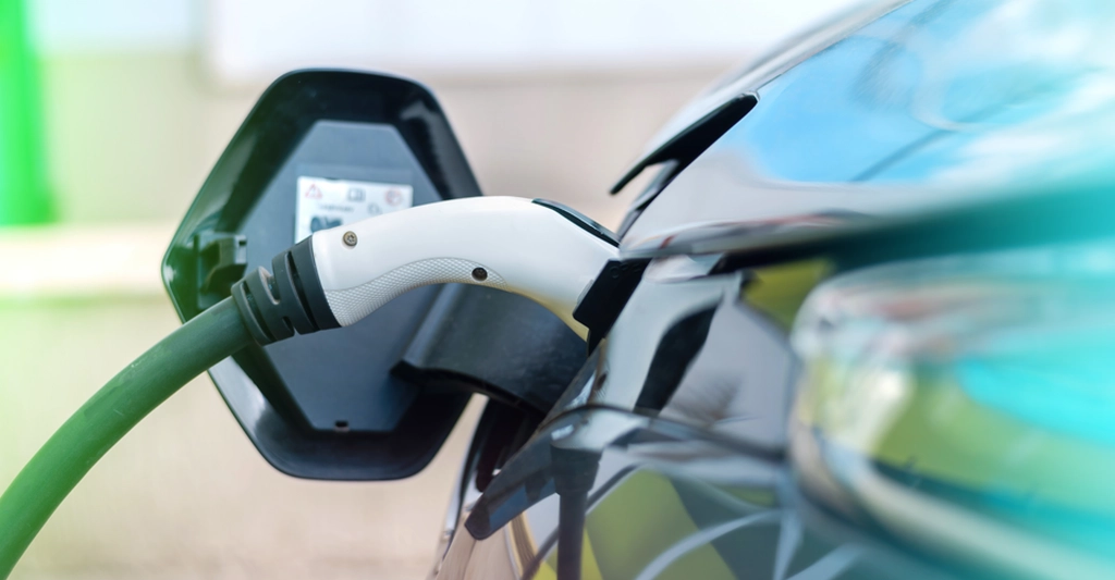 Close-up shot of an electric car being charged, with a green cable plugged into the charging port.