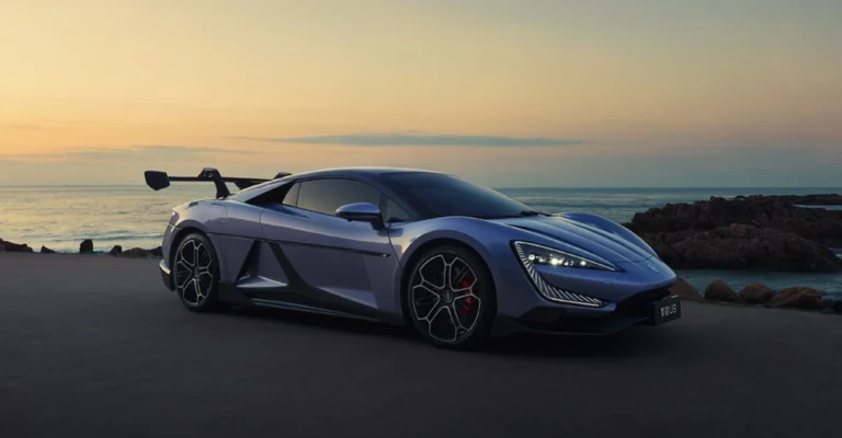 A photograph of a blue The Yangwang U9 sports car parked on a road near the ocean at sunset. The car is sleek and modern, with a low profile and sharp lines