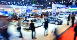 A wide-angle, long exposure shot captures the bustling atmosphere of a car show.