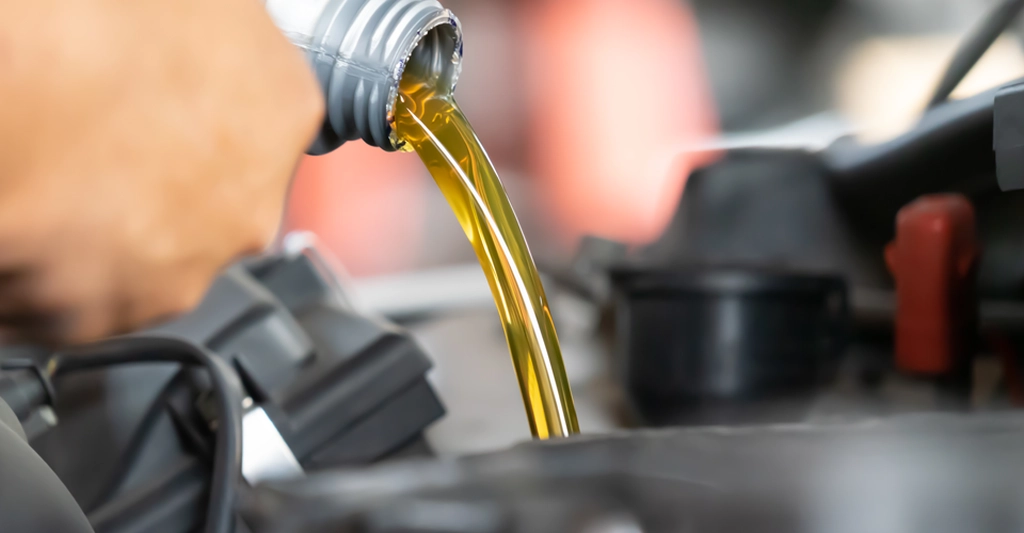 Close-up shot of a hand pouring motor oil from a gray plastic bottle into a car engine