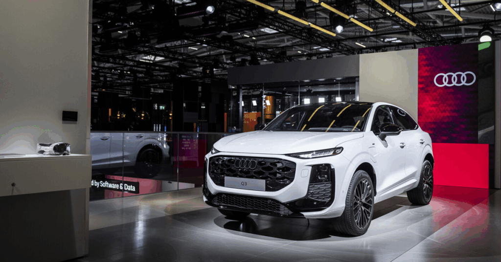 A white Audi Q3 e-tron is displayed on a shiny floor in a showroom. The car has a black grille, black rims, and a black roof.