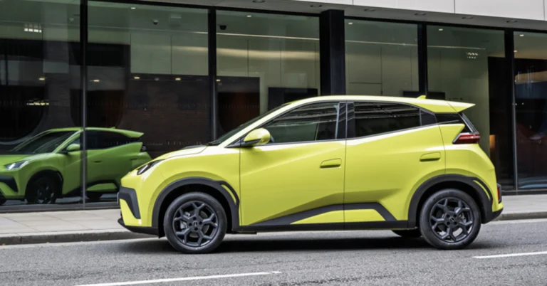 A yellow BYD Dolphin Surf is parked on a city street, with a modern building featuring large glass windows in the background.
