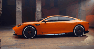 A side view of an orange electric Mercedes Concept AMG GT XX car with black and white wheels, parked inside a building with brick floors and concrete pillars.