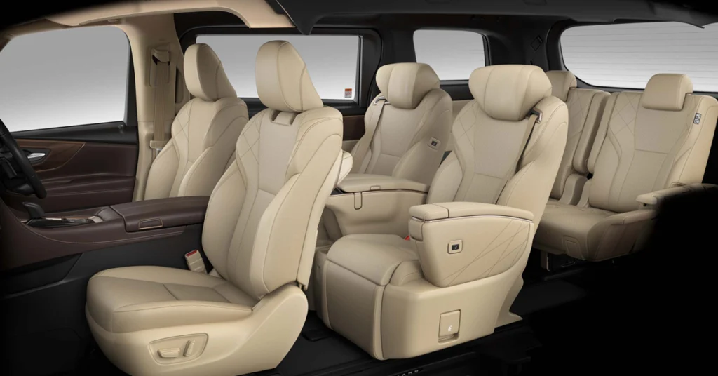 A photograph showcases the interior of a Toyota Alphard, focusing on the seating arrangement. The seats are upholstered in a light beige leather, with a diamond-stitched pattern on the backrests of the rear seats. The front seats have a more contoured design, with adjustable headrests. The interior trim is a dark brown, which contrasts with the light beige of the seats. 