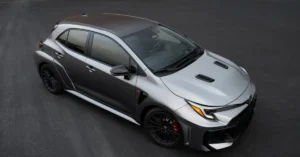 A high-angle shot of a gray and silver Toyota GR Corolla hatchback on a dark asphalt surface. The car has a two-tone color scheme, with the roof and rear section painted in a darker gray, while the front is a lighter silver.