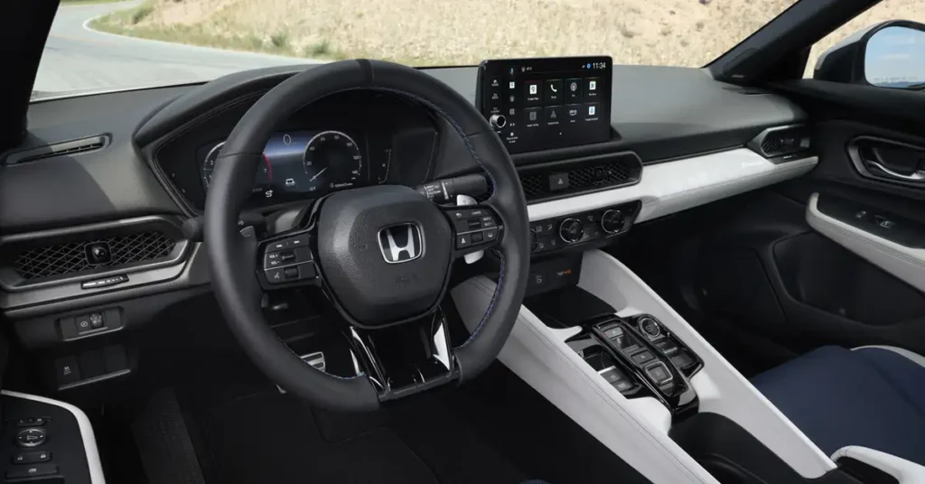 Interior of a 2025 Honda Prelude car, featuring a black leather steering wheel with a silver Honda logo in the center, a digital dashboard display, and a central infotainment screen showing various app icons.