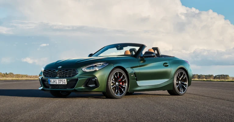 A green BMW Z4 M40i roadster is parked on an asphalt surface under a partly cloudy sky. The car has a sleek, aerodynamic design with a long hood and a short rear deck. The interior is tan leather. The wheels are black with red brake calipers. The car is in excellent condition and appears to be well-maintained.