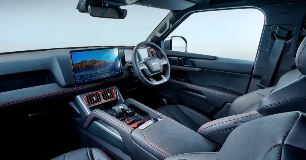Interior of a BYD Shark 6, featuring black leather seats with red stitching, a black dashboard with a large touchscreen display showing a landscape image, a steering wheel with the letters "BYD" on it, and red accents on the air vents and center console, the style is modern and luxurious, with a focus on technology and comfort.