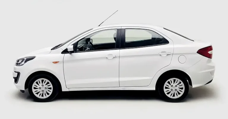 A side view of a white Ford Figo sedan car against a white background. The car has a sleek, modern design with a sloping roofline and a short rear deck. The wheels are silver with a multi-spoke design. The car is well-lit, and the white paint is clean and shiny.