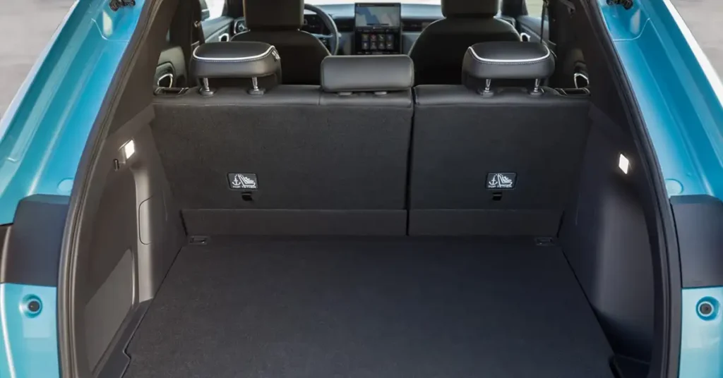 The interior of a Honda N-ONE e car trunk, featuring a black carpeted floor and a teal exterior. The back seats are folded down, revealing a black fabric surface with headrests.
