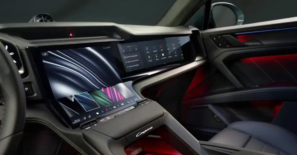A detailed shot of the interior of a Porsche Cayenne, focusing on the dashboard and center console. The dashboard features a sleek, modern design with a large, integrated touchscreen display that spans across the center.