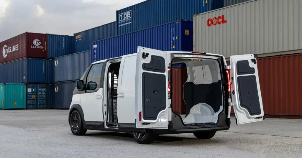 A white Kia PV5: Redefining the Future of Everyday Mobility electric van with its doors open, parked in front of a stack of shipping containers. The van is facing away from the viewer, and its doors are open, revealing the interior.
